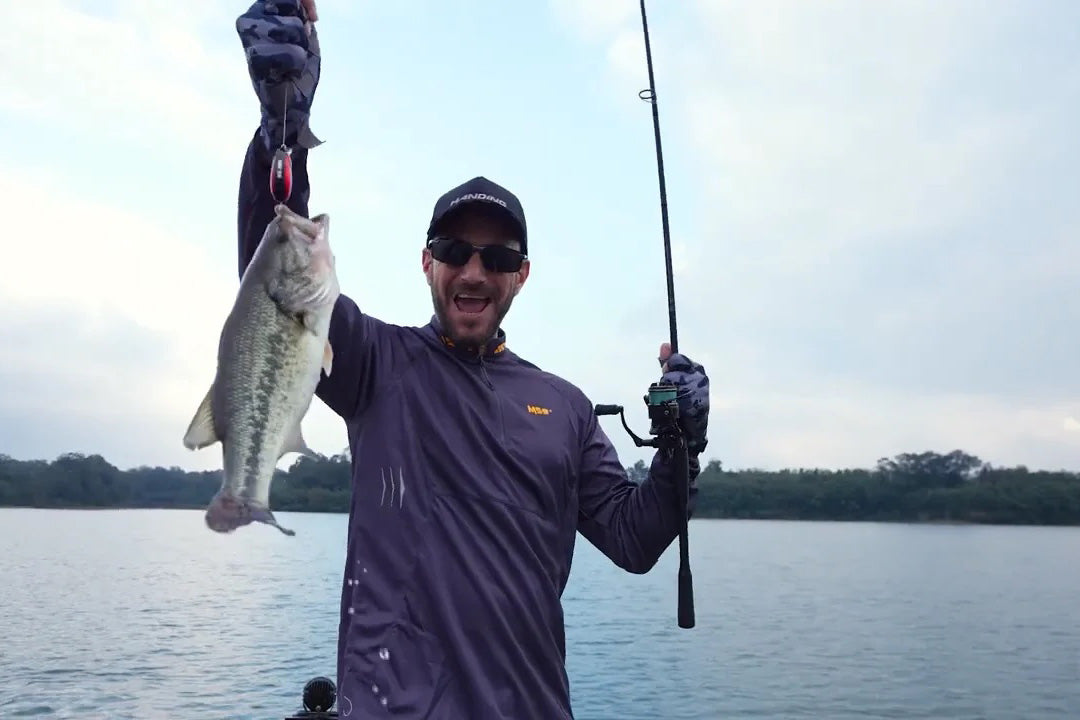 Angler displaying largemouth bass caught during early spring, holding fishing rod and fish by the lake. Caught using slow techniques suitable for early spring water temperatures, showing proper bait selection.